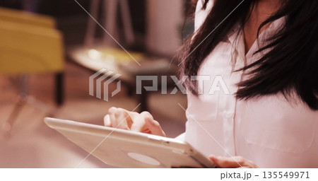 Chinese woman in white button-down shirt tapping tablet screen in modern lounge, with tablet 135549971