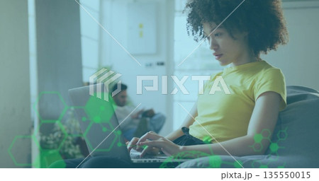 Typing woman using laptop in living room, with potted plant and man using smartphone, copy space 135550015