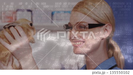 Holding vet wearing scrubs and stethoscope examining brown rabbit in exam room, binary code overlay 135550102