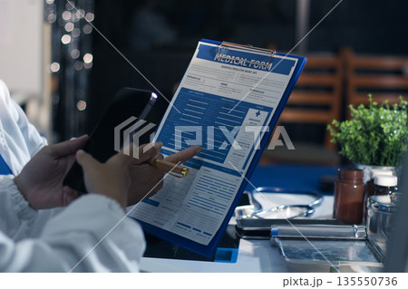 Medical team having a meeting with doctors in white lab coats and surgical scrubs seated at a table discussing a patients working online using computers in the medical industry. Medical team having a meeting with doctors in white lab coats and surgical scrubs seated at a table discussing a patients working online using computers in the medical industry. 135550736