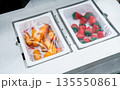 Vacuum sealed food trays with chicken and strawberry inside industrial packaging machine in modern factory. Food processing, hygiene control, automation technology, and safe meal preparation. 135550861