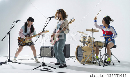 スタンドマイクを使って歌いながら演奏するガールズバンドのメンバーたち スタンドマイクを使って歌いながら演奏するガールズバンドのメンバーたち 135551411