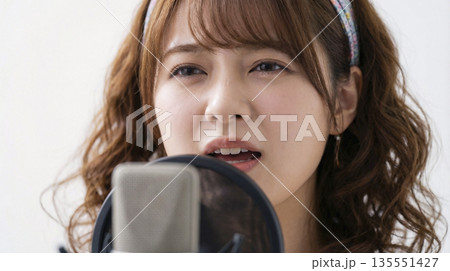 スタジオのマイクに向かって歌う巻き髪の日本人女性歌手の顔のアップ 135551427