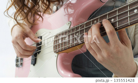 ピンクのエレキベースを演奏する女性の手元と指使いのクローズアップ ピンクのエレキベースを演奏する女性の手元と指使いのクローズアップ 135551428