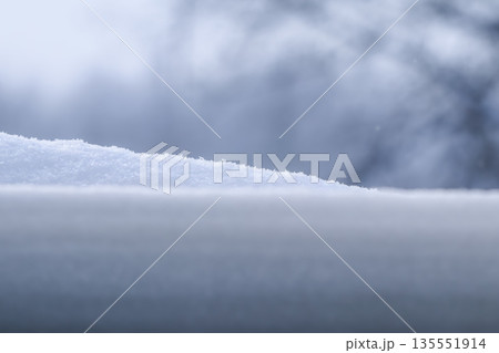 White snow covering a flat surface with a blurred frosty winter background, creating a cool and calm scene 135551914