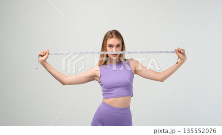 Fit woman stretching measuring tape in studio, body size check, diet and fitness progress concept with copy space background Fit woman stretching measuring tape in studio, body size check, diet and fitness progress concept with copy space background 135552076