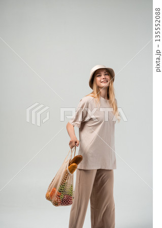 Happy young woman posing with reusable mesh shopping bag full of groceries, sustainable food and modern eco lifestyle concept 135552088