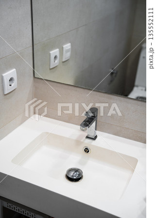 Modern bathroom vanity corner with white sink and chrome faucet, minimalist tiled wall and mirror, home interior and plumbing design concept Modern bathroom vanity corner with white sink and chrome faucet, minimalist tiled wall and mirror, home interior and plumbing design concept 135552111