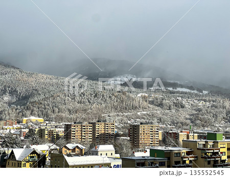 Small town against the backdrop of the Alpine mountains covered with snow-covered forest and clouds Small town against the backdrop of the Alpine mountains covered with snow-covered forest and clouds 135552545