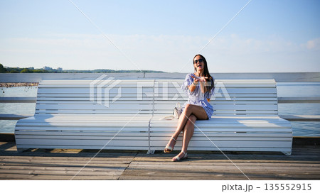 Young woman sitting on bench by sea on sunny summer day Young woman sitting on bench by sea on sunny summer day 135552915