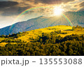 mountainous countryside landscape with rolling hills on summer sunset. rural area in evening light. beautiful view of place with green grassy pastures. storytelling cinematic image under the rainbow 135553088