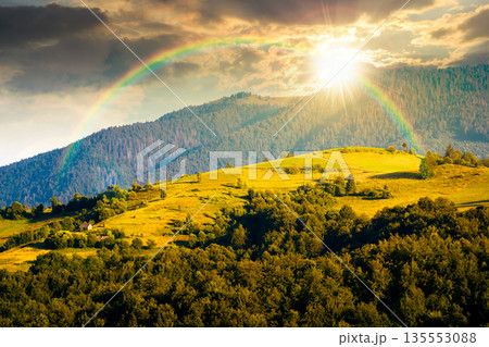 mountainous countryside landscape with rolling hills on summer sunset. rural area in evening light. beautiful view of place with green grassy pastures. storytelling cinematic image under the rainbow 135553088
