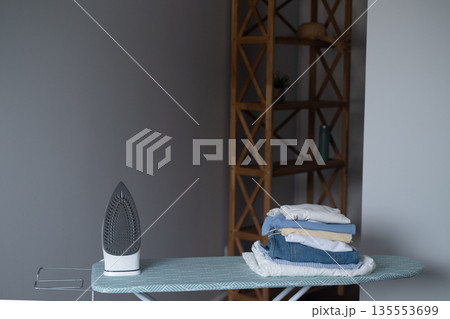 Everyday home comfort with iron on ironing board as a symbol of neatness and order in the household Everyday home comfort with iron on ironing board as a symbol of neatness and order in the household 135553699