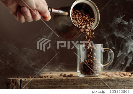 Roasted coffee beans is poured in a clear glass mug. Roasted coffee beans is poured in a clear glass mug. 135553862