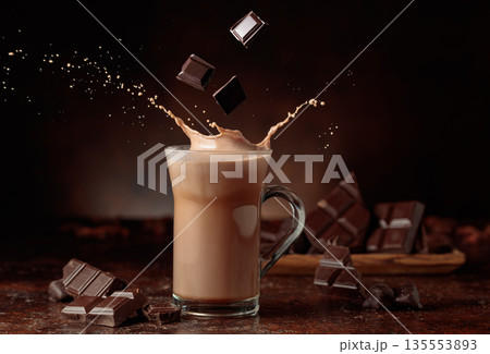 Pieces of bitter chocolate fall in glass mug with cocoa drink. 135553893
