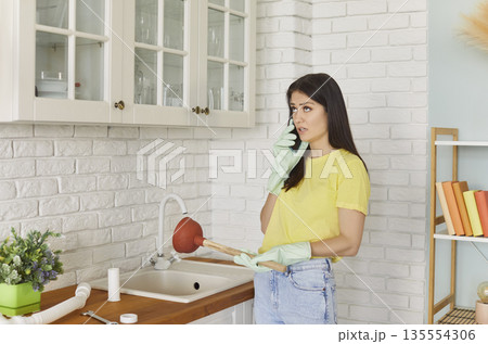 Young girl talking by the phone advising with plumber how to unclog a sink drain. 135554306
