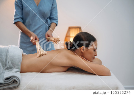 Wooden sticks. Relaxed young woman getting massage by therapist in spa salon Wooden sticks. Relaxed young woman getting massage by therapist in spa salon 135555274