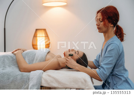 Black roller massager. Relaxed young woman getting massage by therapist in spa salon Black roller massager. Relaxed young woman getting massage by therapist in spa salon 135555313