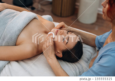 Cleaning the face skin. Relaxed young woman getting massage by therapist in spa salon Cleaning the face skin. Relaxed young woman getting massage by therapist in spa salon 135555315
