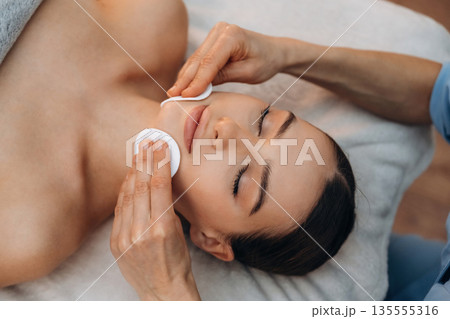 Cleaning the face skin. Relaxed young woman getting massage by therapist in spa salon Cleaning the face skin. Relaxed young woman getting massage by therapist in spa salon 135555316