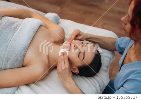 Cleaning the face skin. Relaxed young woman getting massage by therapist in spa salon Cleaning the face skin. Relaxed young woman getting massage by therapist in spa salon 135555317