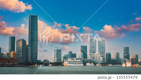 Cruise ship docked at waterfront with modern glass skyscrapers and historic red brick buildings during daytime, showing urban harbor with clear water under overcast sky 135555479