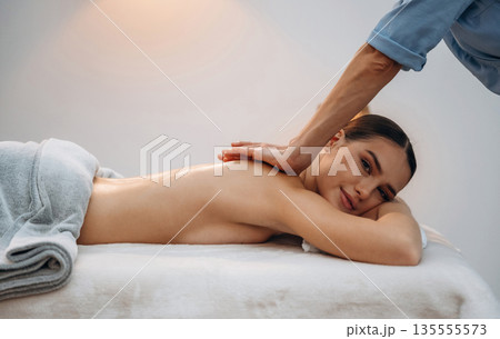 Using oil. Relaxed young woman getting massage by therapist in spa salon Using oil. Relaxed young woman getting massage by therapist in spa salon 135555573