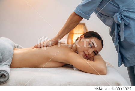 Using oil. Relaxed young woman getting massage by therapist in spa salon Using oil. Relaxed young woman getting massage by therapist in spa salon 135555574