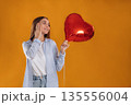 Happy woman with heart shaped balloon against yellow background 135556004