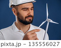 Against blue background. Electrician is holding wind generator toy, conception of eco energy 135556027