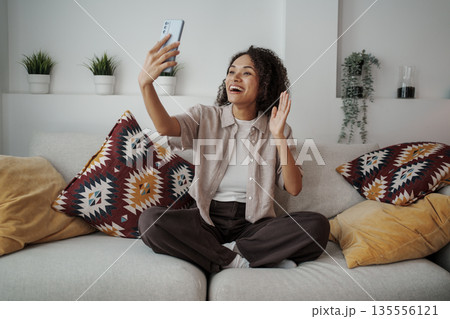 Smiling Woman Greets Friends Remotely, Woman From Her Living Room Waves Happily During Video Interaction Smiling Woman Greets Friends Remotely, Woman From Her Living Room Waves Happily During Video Interaction 135556121