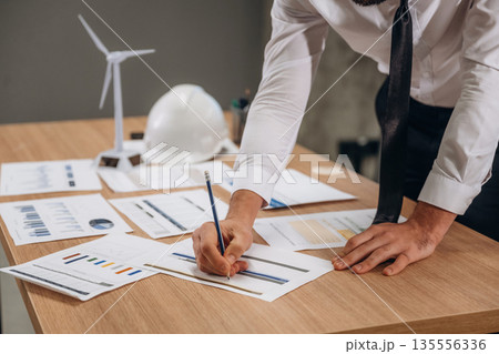 By the table with documents. Man is working in the wind turbine company 135556336