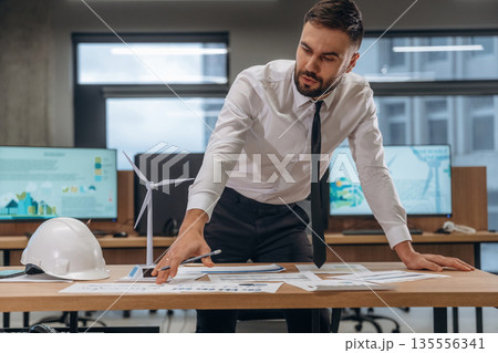 White hardhat and documents on table. Man is working in the wind turbine company White hardhat and documents on table. Man is working in the wind turbine company 135556341