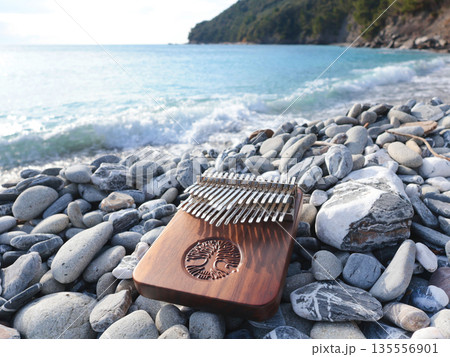 Kalimba musical instrument on stones by sea. Nature near mountains, music, and meditation. Relaxation and mental health.  135556901