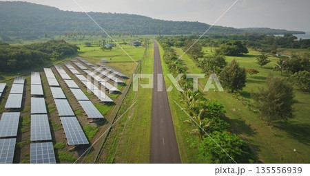 Fiji, Port Villa: solar electric panels along the road, surrounded by green fields and distant hills on Efate Island. Sustainable energy wild nature landscape. Aerial view drone flight 135556939