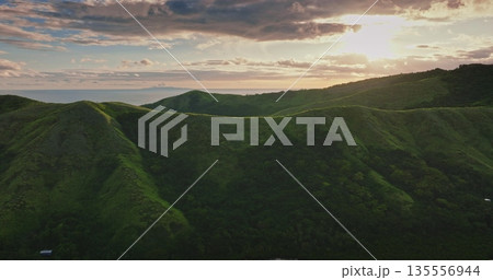 Lush green hills and valleys creating a beautiful landscape in Fiji, with the Pacific Ocean visible in the distance under a dramatic sky with golden sunset light 135556944