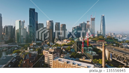 Australia, Sydney: Sydney's cityscape aerial view with tall skyscrapers buildings, construction cranes, streets, traffic road, bridge and modern architecture in morning light. Drone flight panorama Australia, Sydney: Sydney's cityscape aerial view with tall skyscrapers buildings, construction cranes, streets, traffic road, bridge and modern architecture in morning light. Drone flight panorama 135556945