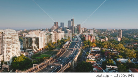 Australia, Sydney: Sydney's skyline at sunrise, skyscrapers, cars driving highway road, residential buildings, and green spaces. Aerial drone flight over modern cityscape, urban architecture Australia, Sydney: Sydney's skyline at sunrise, skyscrapers, cars driving highway road, residential buildings, and green spaces. Aerial drone flight over modern cityscape, urban architecture 135556949