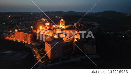 Malta, Comino island: Warm lights illuminating the Cittadella in Gozo at twilight, creating magical atmosphere reflecting Maltese history and old architecture at night. Aerial drone flight Malta, Comino island: Warm lights illuminating the Cittadella in Gozo at twilight, creating magical atmosphere reflecting Maltese history and old architecture at night. Aerial drone flight 135556958