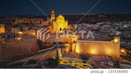 Malta, Comino island: Majestically illuminated historic Citadel in Gozo. The ancient fortifications glow beautifully in the night electric lights. Aerial view drone flight rotation panorama Malta, Comino island: Majestically illuminated historic Citadel in Gozo. The ancient fortifications glow beautifully in the night electric lights. Aerial view drone flight rotation panorama 135556980