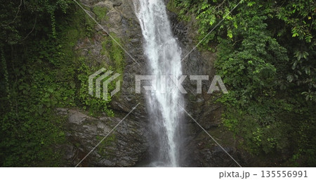 Fiji, Nadi Waterfall: Crystal clear water cascading down a moss covered cliff, surrounded by lush greenery, creates a breathtaking rainforest scene. Wild nature landscape. Drone flight zoom in Fiji, Nadi Waterfall: Crystal clear water cascading down a moss covered cliff, surrounded by lush greenery, creates a breathtaking rainforest scene. Wild nature landscape. Drone flight zoom in 135556991