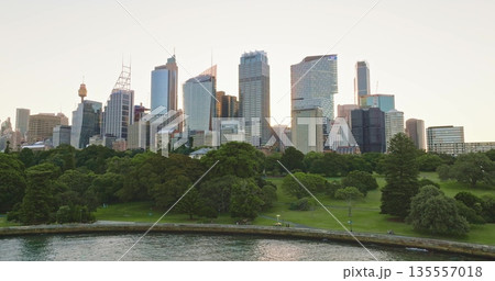Australia, Sydney: Sydney's modern skyline, highlighted by iconic Sydney Tower, rises above the lush Royal Botanic Garden, creating a stunning contrast during a vibrant sunset. Drone flight Australia, Sydney: Sydney's modern skyline, highlighted by iconic Sydney Tower, rises above the lush Royal Botanic Garden, creating a stunning contrast during a vibrant sunset. Drone flight 135557018
