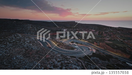 Malta: Breathtaking aerial view of cars driving along winding coastal road in Malta during a vibrant sunset, showcasing the island's beautiful landscape and the Mediterranean Sea. Drone flight Malta: Breathtaking aerial view of cars driving along winding coastal road in Malta during a vibrant sunset, showcasing the island's beautiful landscape and the Mediterranean Sea. Drone flight 135557038