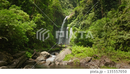 Sendang Gile waterfall in Lombok. Water cascade flowing into a rocky river, surrounded by lush tropical jungle and green vegetation, with people swim, relax, enjoy nature beauty. Drone flight 135557050