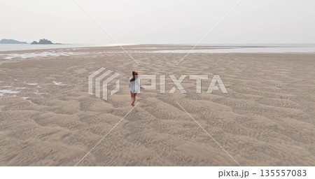 Woman running on Ko Lanta beach during low tide, finding freedom and vastness across rippled sand patterns extending towards the calm ocean and distant islands. Aerial drone flight, back view Woman running on Ko Lanta beach during low tide, finding freedom and vastness across rippled sand patterns extending towards the calm ocean and distant islands. Aerial drone flight, back view 135557083