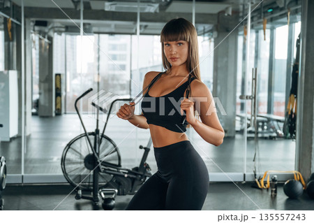 Jumping rope in hands and on the neck. Young woman is in the gym Jumping rope in hands and on the neck. Young woman is in the gym 135557243