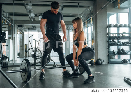 Squats with dumbbell. Man and woman are in the gym together Squats with dumbbell. Man and woman are in the gym together 135557353