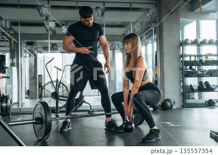 Squats with dumbbell. Man and woman are in the gym together 135557354
