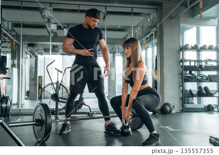 Squats with dumbbell. Man and woman are in the gym together Squats with dumbbell. Man and woman are in the gym together 135557355