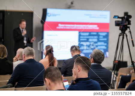 Business conference presentation with speaker audience and video crew in a modern seminar hall 135557824